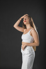 Modelo mujer joven de pelo largo posando con top blanco y pantal&oacute;n blanco sobre fondo negro.