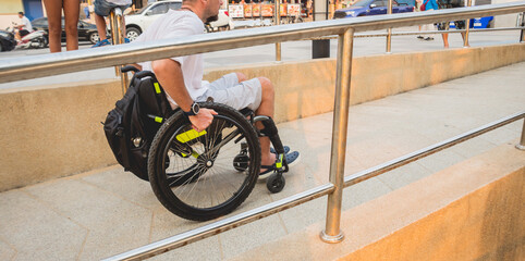 Disabled man in a wheelchair moves on a ramp to the beach.