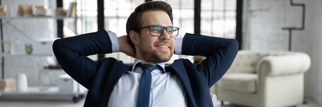 Horizontal panoramic view of smiling young Caucasian businessman look in distance relax at workplace, happy male employer or boss dreaming thinking in office, business vision, success concept