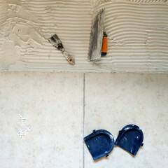 Installation of  ceramic tiles. Tools for laying tiles- trowel, toothed spatula, plastic crosses, knee pads. Glue for a tile with a gear pattern.  Renovation or repair concept.