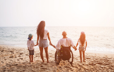 Disabled man in a wheelchair with his family on the beach.