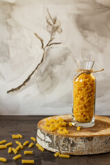 Spiral pasta in a glass jar on a wooden stand, scattered on the table