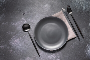 Empty black plate and cutlery set on black rustic table top view, copy space for your design. 