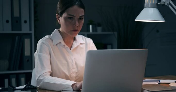 Tired Businesswoman Closing Down Her Laptop And Banging Head On Arms Late Night At Office