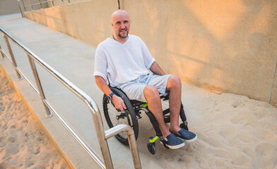 Obraz premium Disabled man in a wheelchair moves on a ramp to the beach.