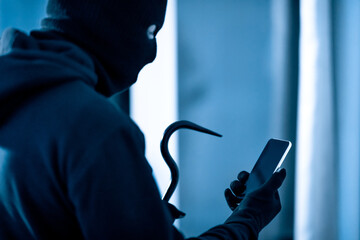 Villain holding crowbar and smartphone preparing burglary
