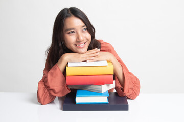 Happy young Asian woman read a book with books on table .