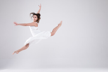 Dancer in jump girl in a white dress, a girl on a light background, brunette in a white dress Portrait of girl in white clothes. Gymnastics, dance, preparation, contemporary, practice, workout