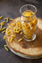 Spiral pasta in a glass jar on a wooden stand, scattered on the table