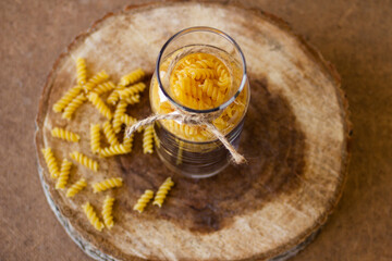 Spiral pasta in a glass jar on a wooden stand, scattered on the table