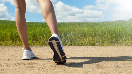 Fototapeta na wymiar Close-up of the legs of a female runner against a green field. Summer training