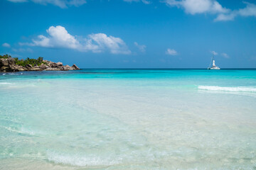 Ocean waves, white boat, pristine blue color lagoon and granite rocks on Anse Coco beach, La Digue Island, Seychelles