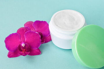 Cream in white jar with green cap on mint background with beautiful bright magenta orchid flowers. Soft cream with orchid extract for moisturizing skin. Eco cosmetic product
