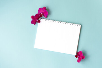 Top view of empty notebook with white pages and bright pink orchid flowers on mint background.Natural mock up with tropical flowers