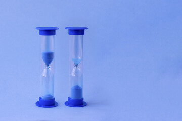 Two hourglass with falling sand inside of them as a symbol of running time, lifetime and no time. Sand watches with a big and little amount of blue sand as metaphor of rushing time.
