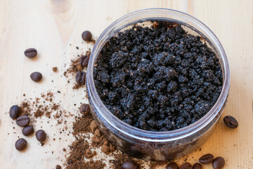 Bowl full of ground coffee scrub with olive oil and salt as homemade facial and body scrub on wooden background with roasted coffee beans. Homemade cosmetics for peeling and rejuvenation,