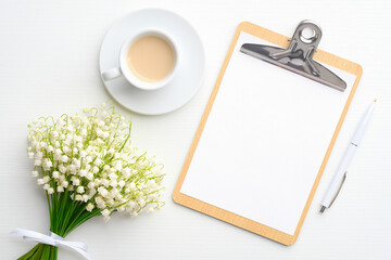 Flat lay composition with blank paper clipboard, coffee mug and bouquet of flowers lily of the valley, view from above. Wedding planning concept.