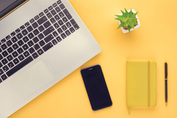 notebook, laptop, pen, flower, mobile phone on a yellow surface