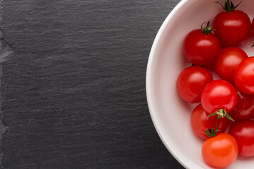 Cherry tomatoes in a white bowl on a stone black board with water drops.