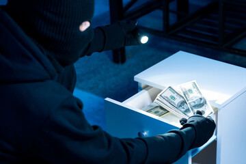 Robber stealing money from drawer, using flashlight