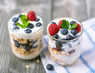 White yogurt in glass jar with fruits on grey background.
