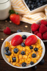 Corn flakes with blueberries and raspberries in white bowl in dark wooden desk.