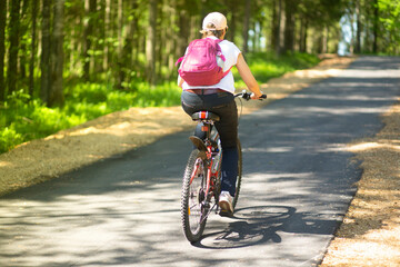 A woman rides a Bicycle on an asphalt road in the Park in the summer.