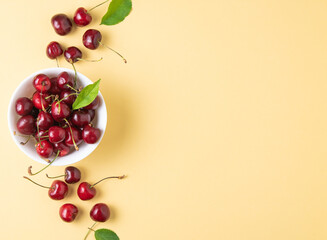 juicy cherries and leaves in white bowl on a yellow background