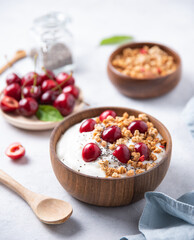 natural fermented yogurt with granola, chia seeds  and  cherry in wood bowl on light table