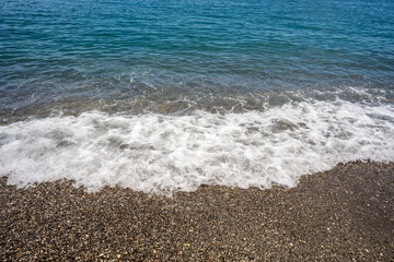 Foamy wave reaching a calm beach with sand and pebbles. Front view copy space.