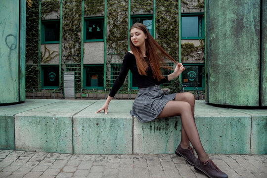Stylish girl in black sweaters and short skirts posing near the building of the Library of the University of Warsaw. Young woman model appearance with long hair.