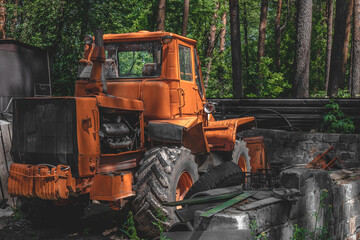 old big orange tractor abandoned in a pine forest. big wheels. The shadow of the trees in the cabin. Technology and nature