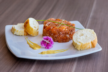 Homemade Salmon Tartare dish by amateur chef for culinary blogs, decorated with eatable purple flower and mostard.