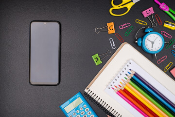 Time for school concept. Top above overhead view photo of colorful stationery and a phone with empty touch screen for copyspace isolated on blackboard
