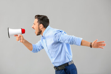 Screaming young businessman with megaphone on grey background