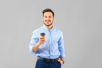 Handsome young businessman with coffee on grey background