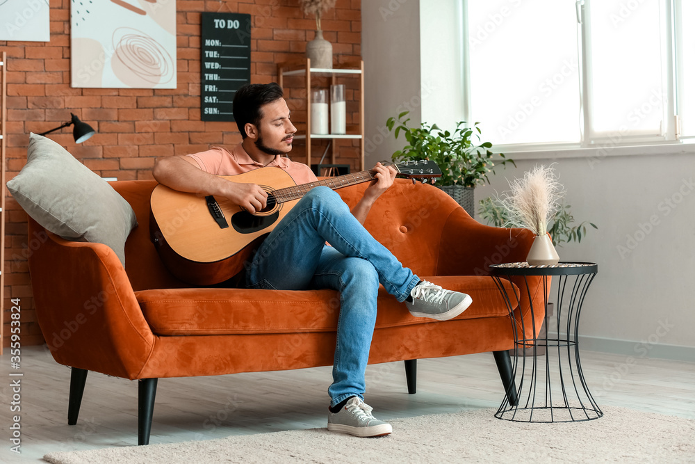 Wall mural Handsome young man playing guitar at home