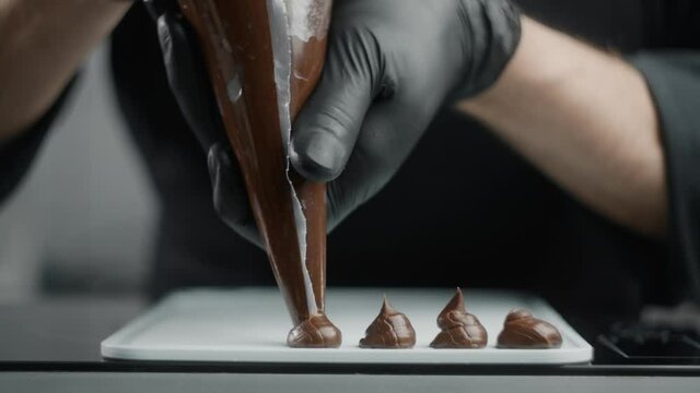Chef chocolatier makes sweets from melted chocolate with pastry bag in slow motion, raw materials for making filling for truffles, cooking the sweet desserts, making candies, Full HD 240 fps Prores HQ