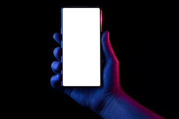 Phone in hand. Silhouette of male hand lit with blue and red neon lights holding bezel-less smartphone on black background. Screen is cut with clipping path. - 355955203
