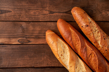 Three crispy french baguettes lie on an old wooden table with free space for text