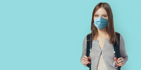 Student woman wearing face mask standing against blue wall with backpack. Safe back to school...
