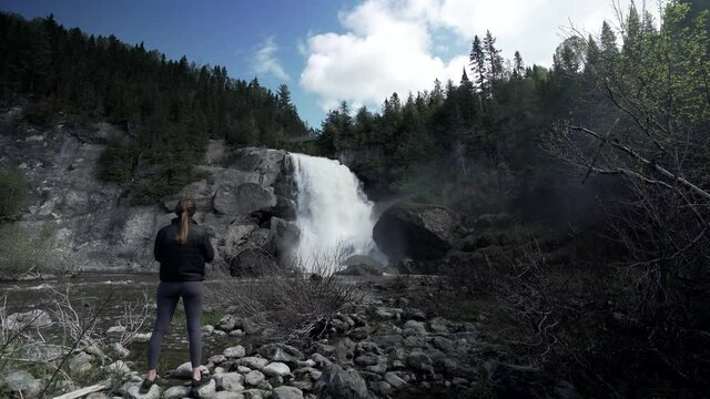 Chute Neigette, Rimouski In Quebec, Canada - Tourist Standing In Front Of A Beautiful Waterfall Taking Photos Using Her Cellphone - Medium Shot