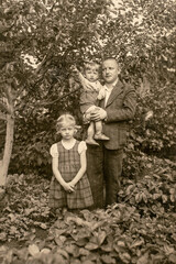 Latvia - CIRCA 1930s: Portrait of father with two children in garden. Vintage archive Art Deco era photography