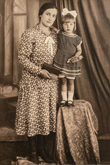Latvia - CIRCA 1930s: Portrait of mother and daughter standing on bench in studio, Vintage archive Art Deco era photo