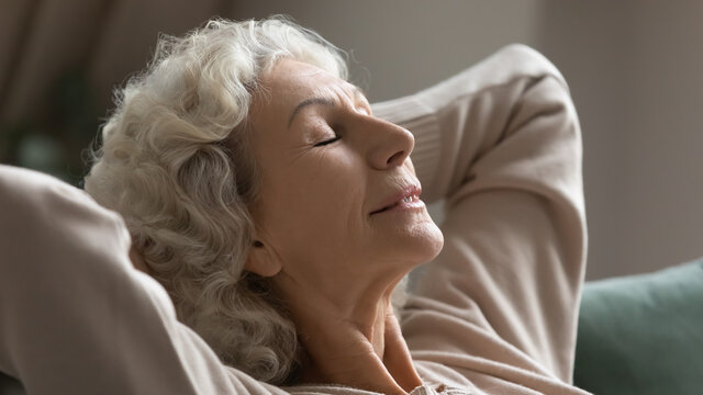 Close Up Of Happy Calm Elderly Female Relax On Comfortable Sofa At Home Sleeping Or Taking Nap, Smiling Peaceful Mature Woman Rest On Couch, Breathe Fresh Air Or Meditate, Stress Free, Peace Concept