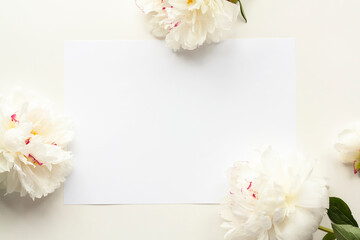 Flower composition made of white peonies and blank sheet of paper on beige background. Women's Day, Mother's Day, wedding delicate floral background. Flat lay, top view, copy space, mock up.