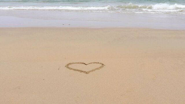 Heart drawn in the golden sand on a beach with soft waves washing behind. Set on a beautiful Scottish beach at Fraserburgh.