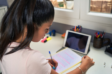Young Latina studying and performing class assignments online with his computer from home for causes of coronavirus. Sitting at her table with leaves and pens. Videoconferencia con sus profesores.