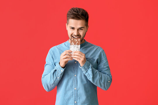 Handsome young man with tasty chocolate on color background