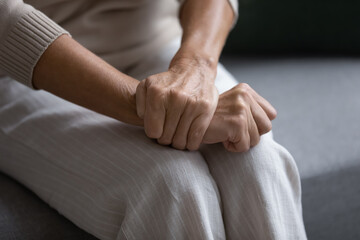 Close up of elderly woman sit on sofa with hands clenched joined on laps making difficult decision,...
